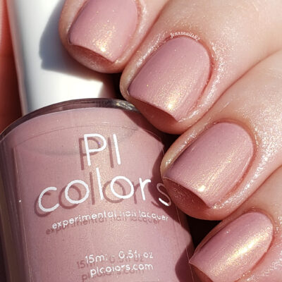 Close-up of a hand with neatly manicured nails painted in a shimmery light pink hue, courtesy of PI Colors' Milk Berry.073 Pink Nail Polish. The bottle is held gracefully between the fingers, showcasing the brand and casting a gentle reflection on its surface.
