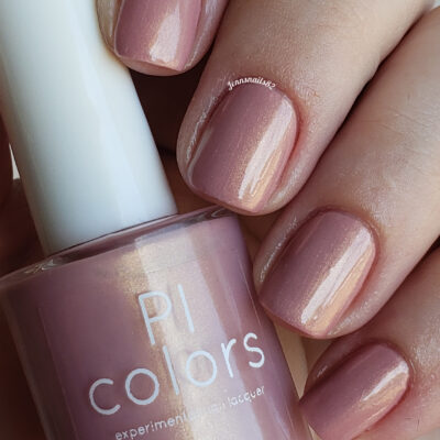 Close-up of a hand with nails painted in a soft, shimmery pink polish. The luxury PI Colors nail lacquer bottle matches the nail color and is charmingly named "Milk Berry.073," featuring a stylish white cap.