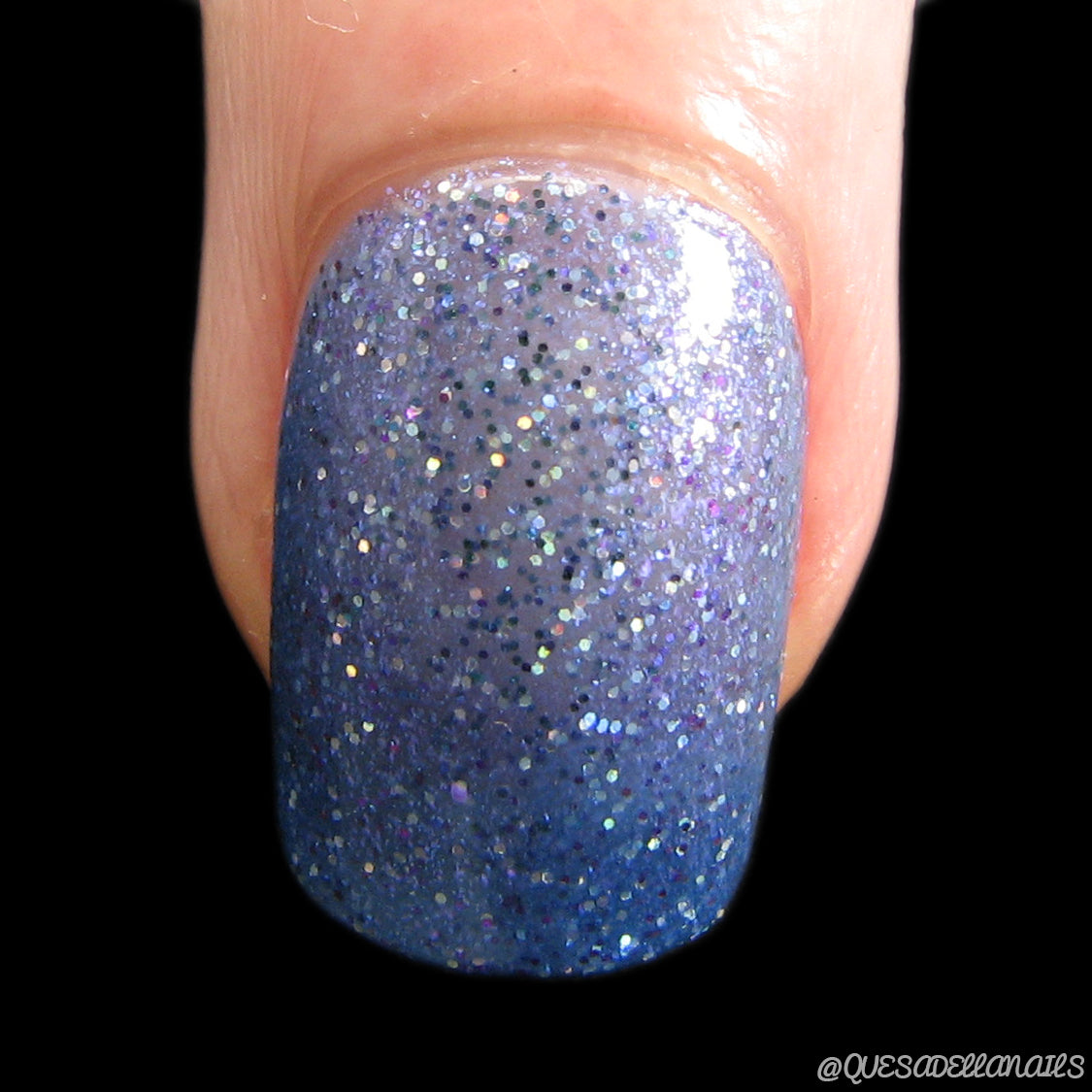 The black background beautifully highlights a close-up of a fingernail painted with PI Colors' Cockatoo.036 Blue Nail Polish. The glossy finish features a luxurious mix of glittery blue and shimmering silver sparkles.