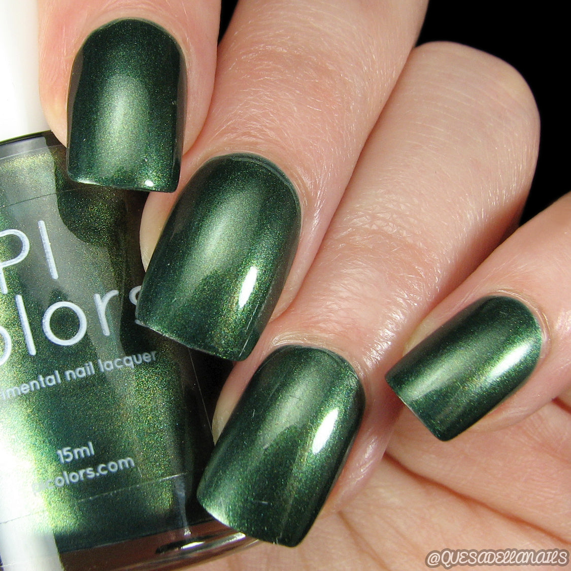 A close-up of manicured nails painted with Juniper Night.001 Green Nail Polish by PI Colors, featuring a metallic forest green shade. The partially visible bottle displays the same striking color. The nails catch the light, enhancing the glossy finish of this 10-free, handmade polish.