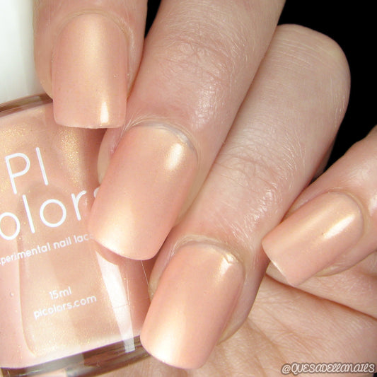 Close-up of a hand with manicured nails painted in a satin peach hue. The glossy luxury of PersiL.007 Peach Nail Polish by PI Colors adds elegance, as the hand holds a beautifully branded bottle.
