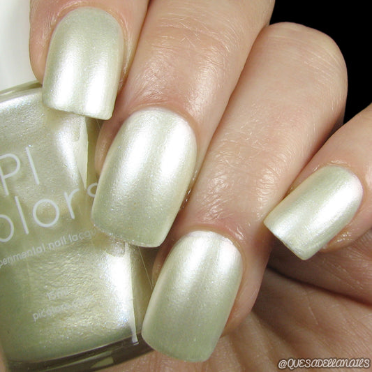 A hand with nails painted in a pearly, iridescent pale green luxury nail lacquer. The PI Colors bottle is partially visible in the background.