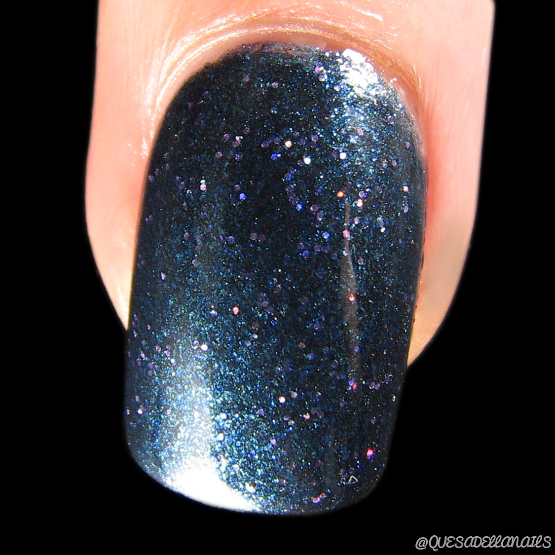 A close-up reveals a fingernail adorned with PI Colors' Watermelon Rind.056 Black Nail Polish, featuring shimmering dark blue hues and tiny holographic glitters. The black background accentuates the glossy finish and sparkle of this 10-free formula.