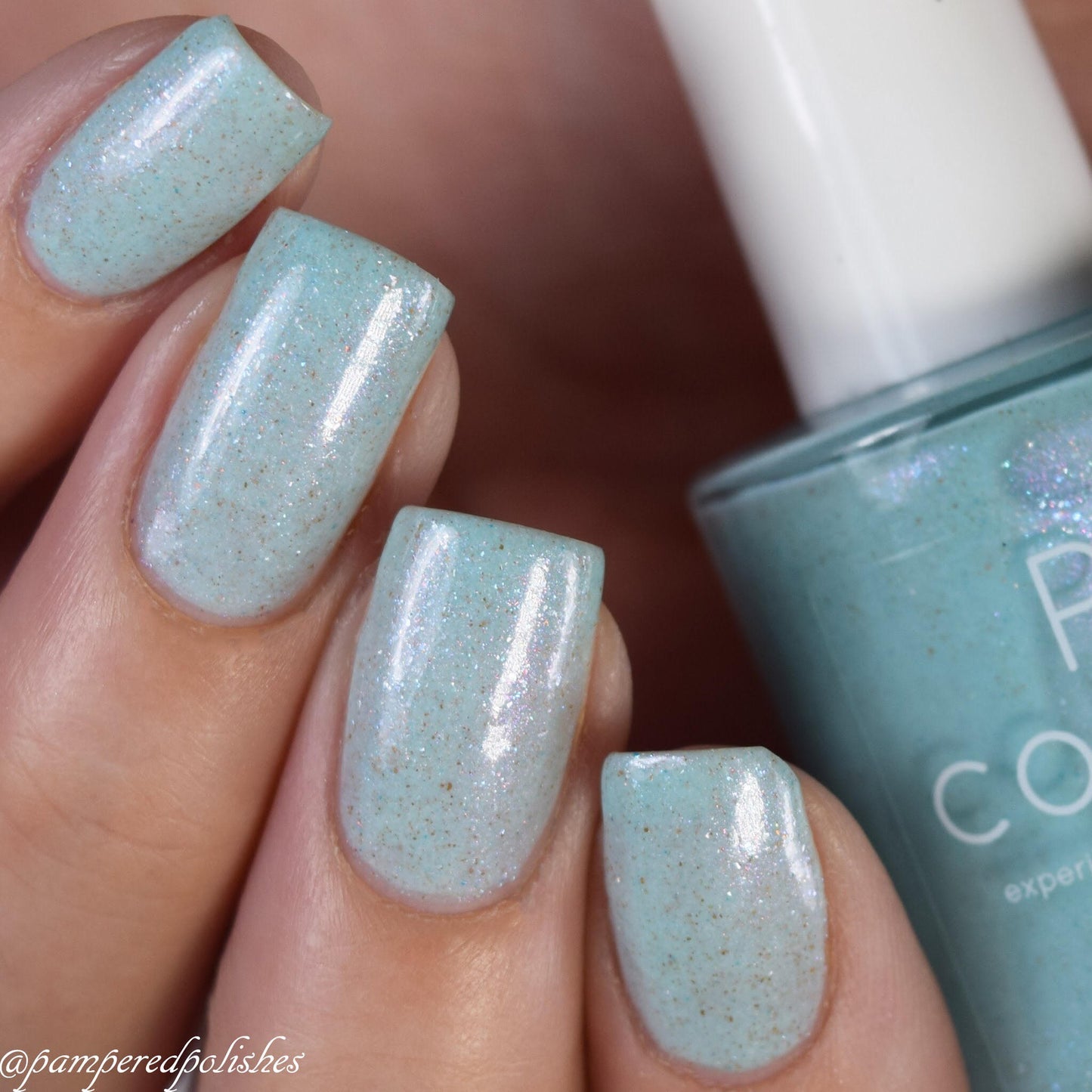 Close-up of a hand adorned with Marshmellow Dream.001 by PI Colors, featuring pale green sparkly nail polish on short, squared nails. The PI Colors Luxury Nail Lacquer bottle appears partially visible on the right, perfectly matching the nail color with a delicate shimmer.