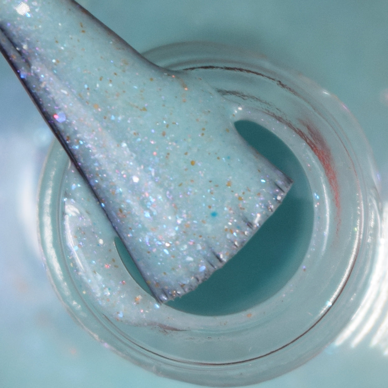 Close-up of a brush dipped in a bottle of Marshmellow Dream.001 by PI Colors. The sparkly pale green polish appears glossy with fine glitter particles, and the brush is coated in the enchanting color-changing liquid, creating a swirling effect around the rim of the bottle.