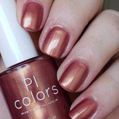 A close-up of a hand with nails painted in Pink Velvet.056 Deep Pink Nail Polish, part of the PI Colors collection. The bottle is elegantly held between the thumb and index finger, perfectly complementing the glossy, shimmering finish on the nails.