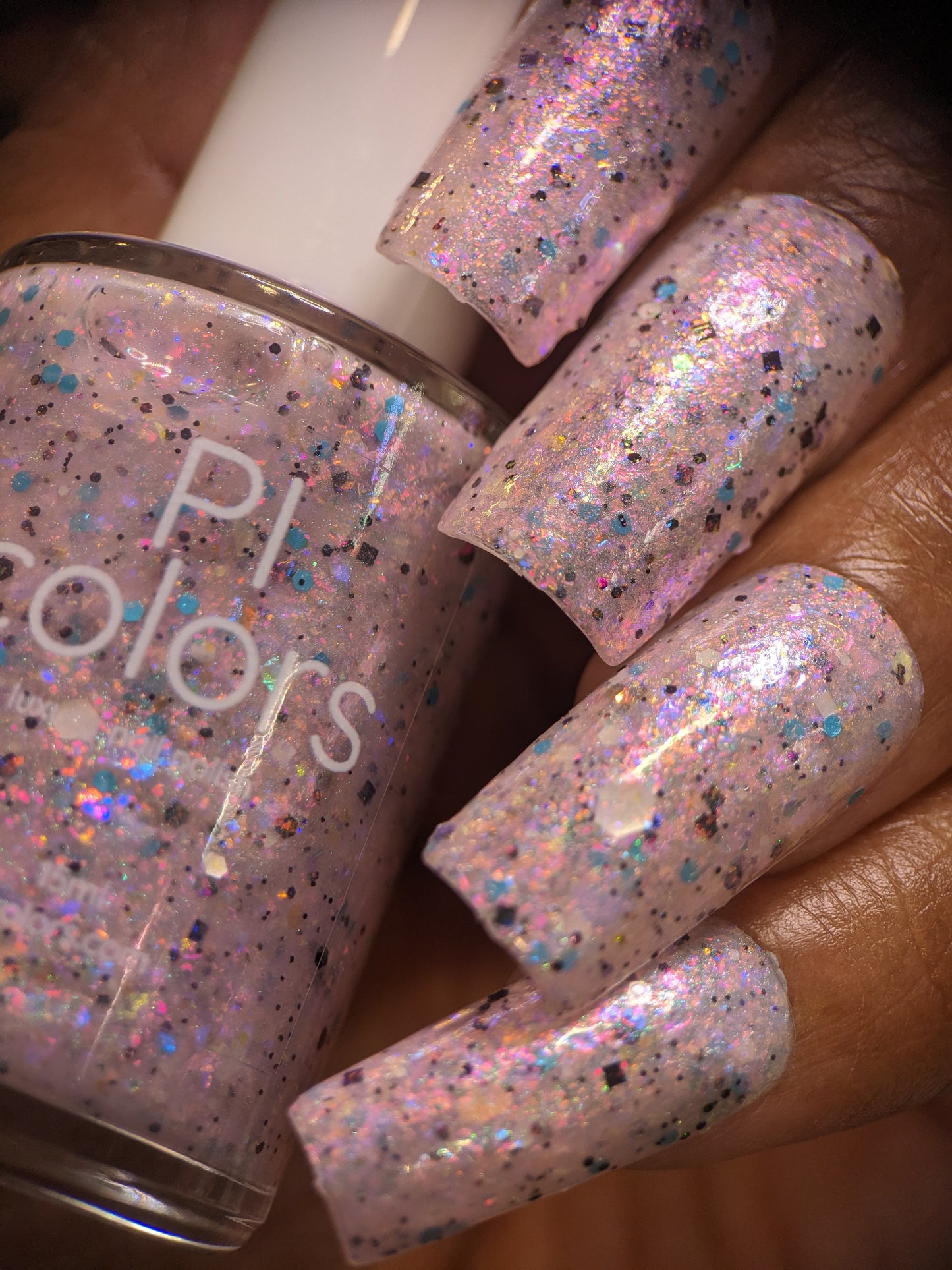 Close-up of fingers with long nails painted in Pink Ash.305 by PI Colors, a shimmery hue with iridescent flakes catching the light. A bottle of this luxurious lacquer is held gently in one hand on the left, highlighting its multicolored brilliance.