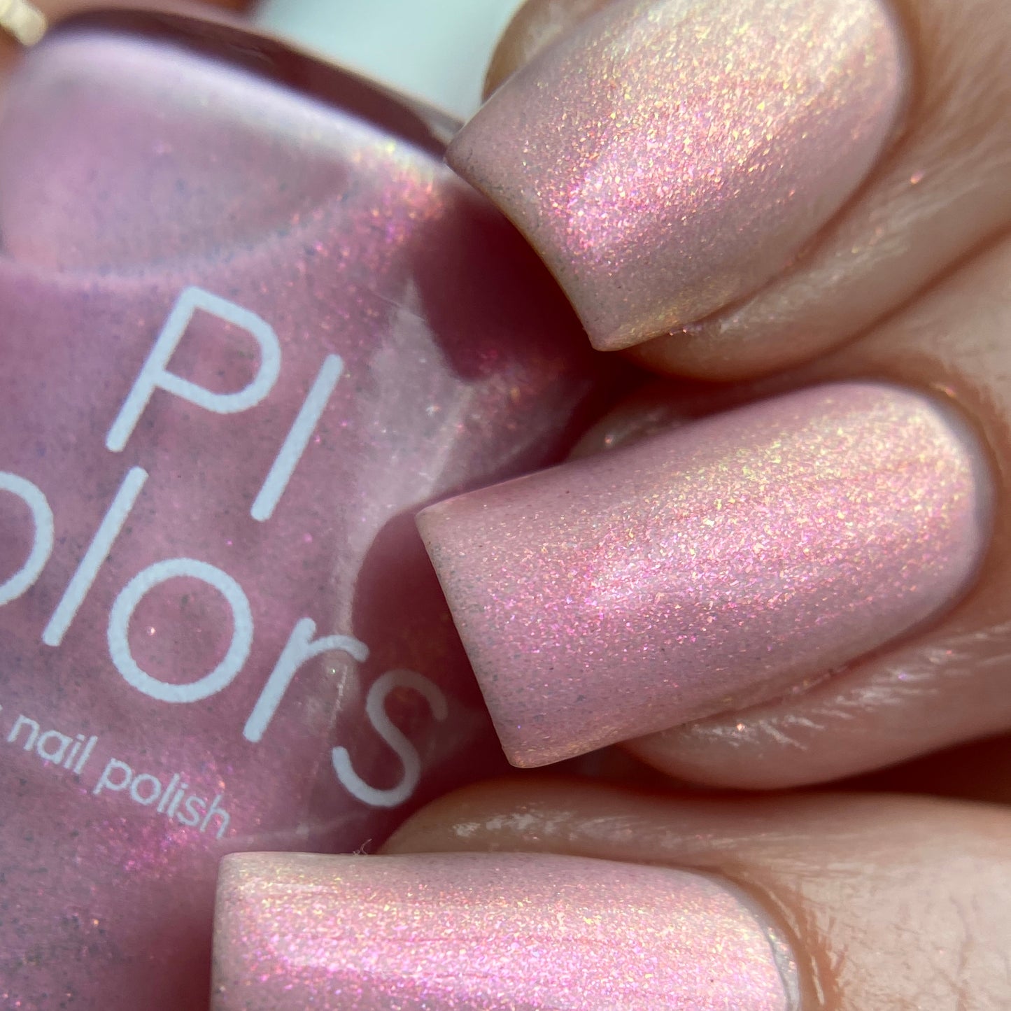 Close-up of nails painted with the luxurious Sunset Aurora.322 Pink Nail Polish. A bottle labeled "PI Colors" is held, showcasing a similar handmade shade. The polish features a subtle glitter effect, giving the nails a glossy and sparkling appearance.