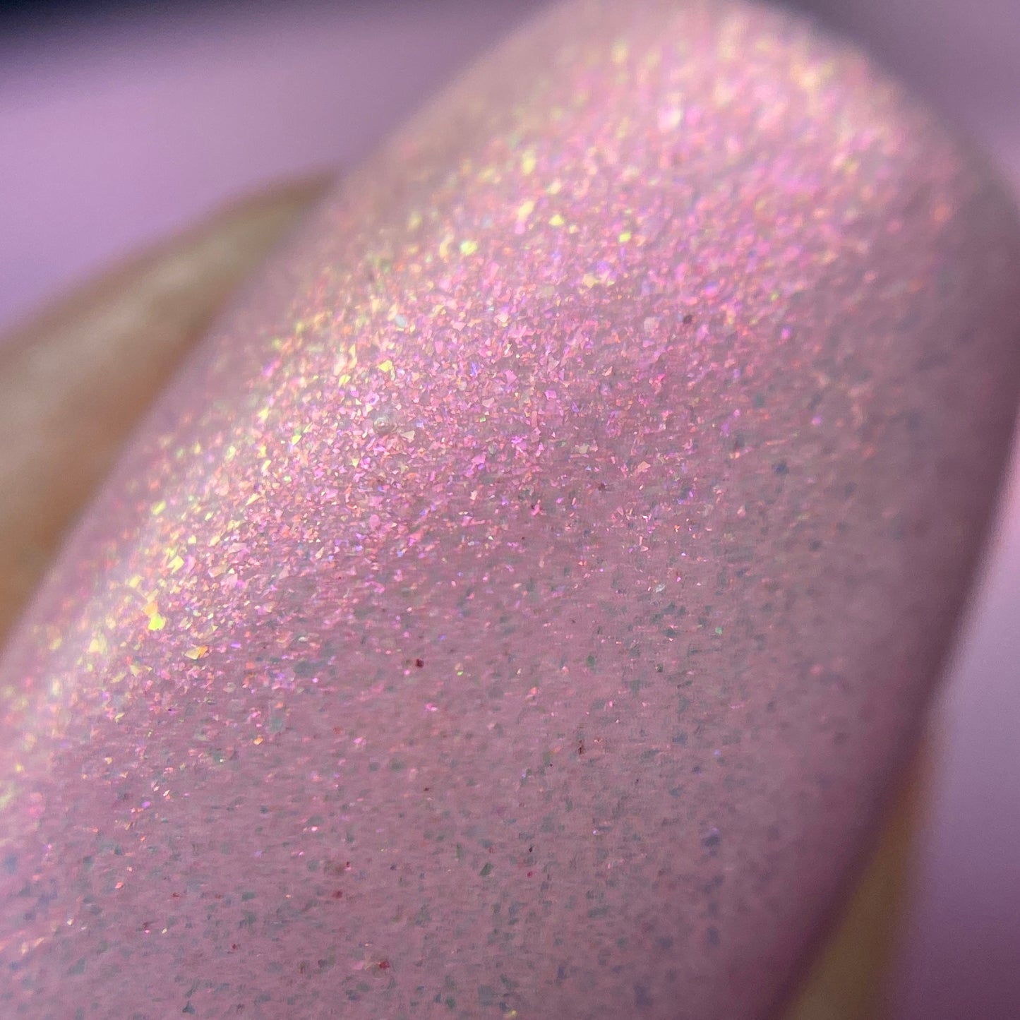 A close-up of a nail embellished with PI Colors' Sunset Aurora.322 Pink Nail Polish, showcasing a handmade shimmer in hues that glisten with iridescent colors. This 10-free luxury lacquer provides a dazzling and textured finish.