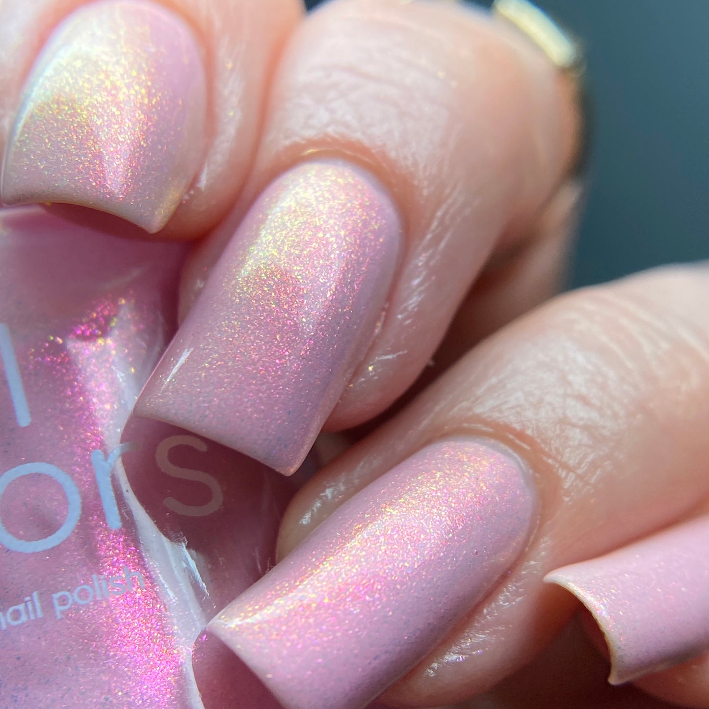 A close-up of hands with long fingernails adorned in PI Colors' opulent Sunset Aurora.322 pink nail polish, holding a bottle of the same exquisite lacquer. The polish features a glossy finish with subtle gold shimmer that dances in the light.
