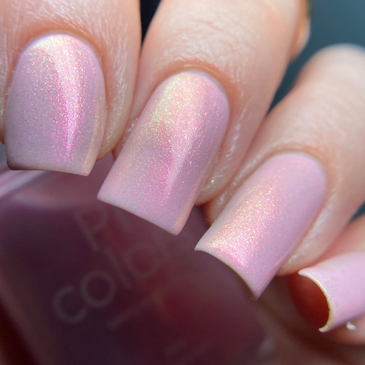 A close-up of fingernails painted with PI Colors' Sunset Aurora.322 Pink Nail Polish showcases a subtle gradient and glossy finish, while the 10-free luxury lacquer bottle is partially visible in the background.