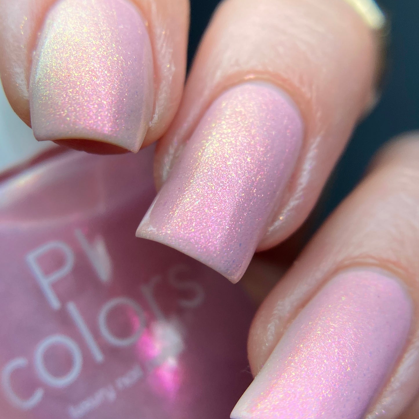 A close-up of a hand showcases nails adorned with PI Colors' Sunset Aurora.322 Pink Nail Polish, creating a glossy and elegant look. A bottle of this 10-free luxury lacquer peeks out in the background, hinting at its refined quality.