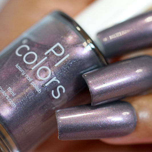 Close-up of a hand holding a nail polish bottle labeled "PI Colors." The nails are painted in the same 10-free, shimmery metallic chrome finish that captures the muted gray purple shade of the Twilight Moon.068 nail polish.