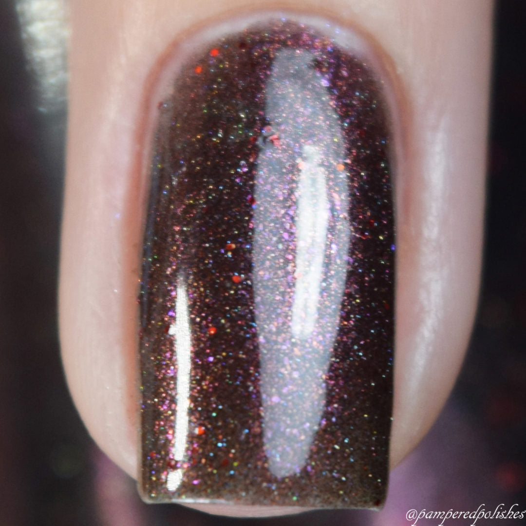 Close-up of a fingernail coated with Ursidae.072 Red Black Nail Polish by PI Colors. This 10-free formula showcases a deep brown base accented with holographic powders for an eye-catching shimmer. The finish is smooth and glossy, beautifully reflecting light.