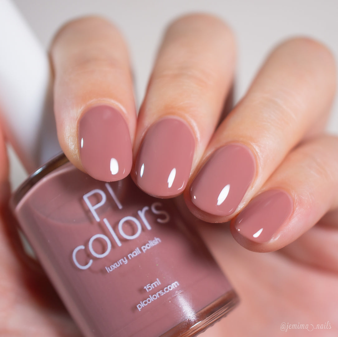 A hand with neatly manicured nails painted in glossy, mauve pink polish holds a matching bottle of PI Colors luxury nail polish.