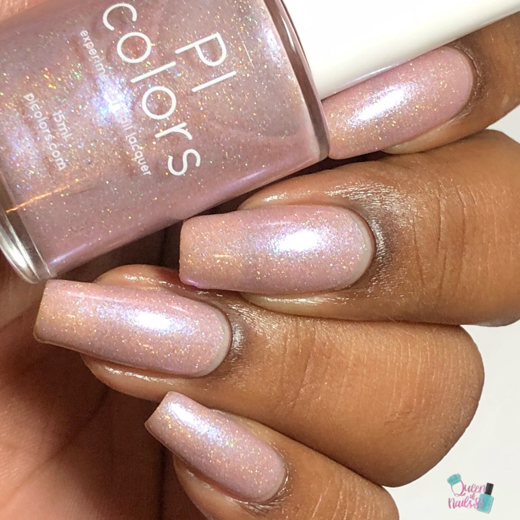 A hand with long, neatly manicured nails painted in a shimmering light pink hue holds a bottle of Moazagotl.127 Pink Nail Polish by PI Colors, showcasing the same delicate color enhanced with holographic glitters.