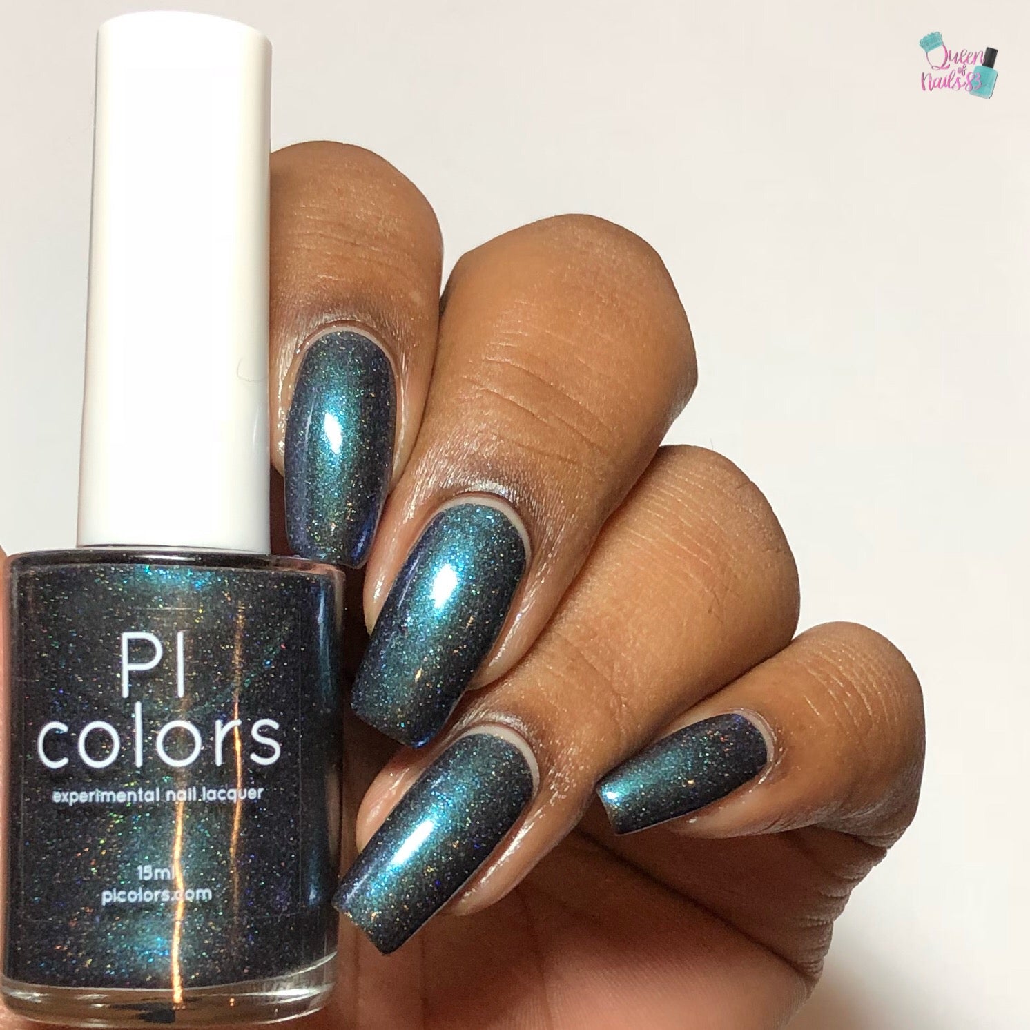 A hand with long nails painted in shimmering dark teal polish holds a bottle of "Noctilucent.111 Black Nail Polish" by PI Colors. This luxury nail lacquer, infused with holographic powders, offers a captivating glow. The bottle perfectly matches the mesmerizing nail color.