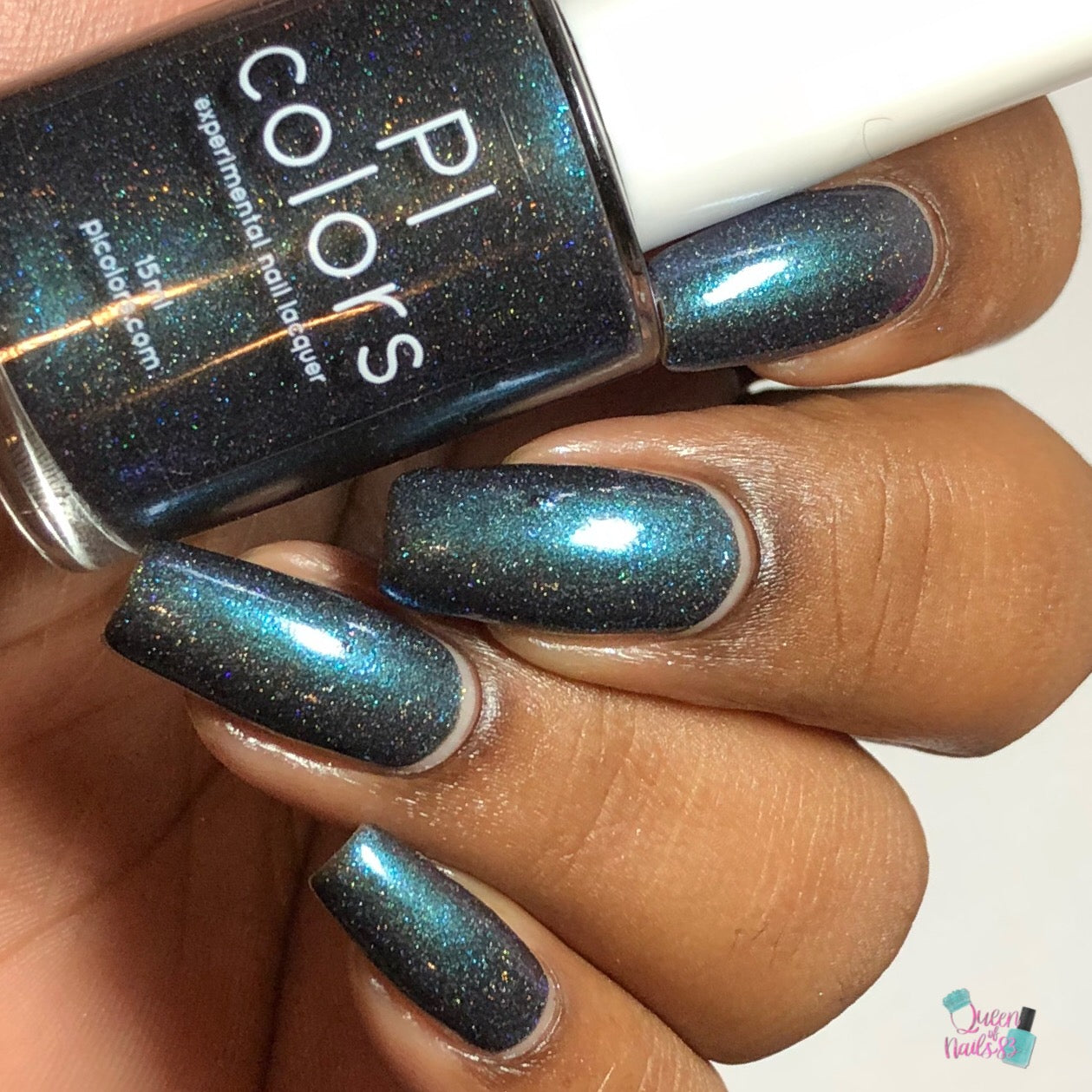 A hand showcases nails adorned with a glossy, dark teal polish from PI Colors, featuring the Noctilucent.111 Black Nail Polish, which adds a subtle sparkle. The bottle of PI Colors nail lacquer aligns perfectly with the vibrant look of the Noctilucent polish.