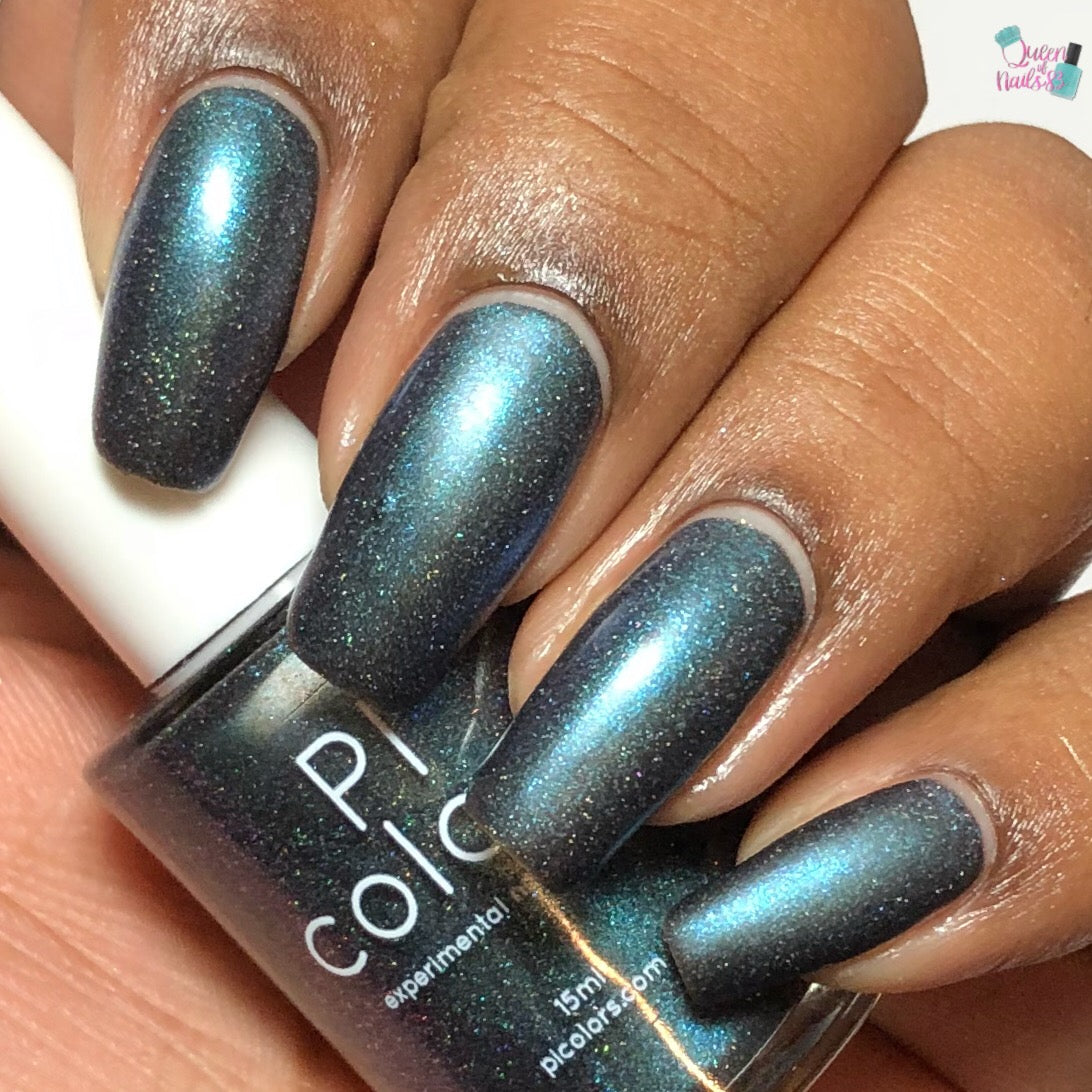 A hand with medium skin tone showcases long nails adorned in a shimmering dark teal nail polish, enhanced with holographic powders. In the background, the "Noctilucent.111 Black Nail Polish" by PI Colors is partially visible.