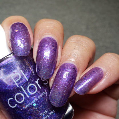 A close-up of a hand with long fingernails painted in Purple Smoke.001 nail polish, shimmering with holo glitters. The PI Colors bottle is held in the same hand, perfectly showcasing its vibrant shade and sparkling finish.