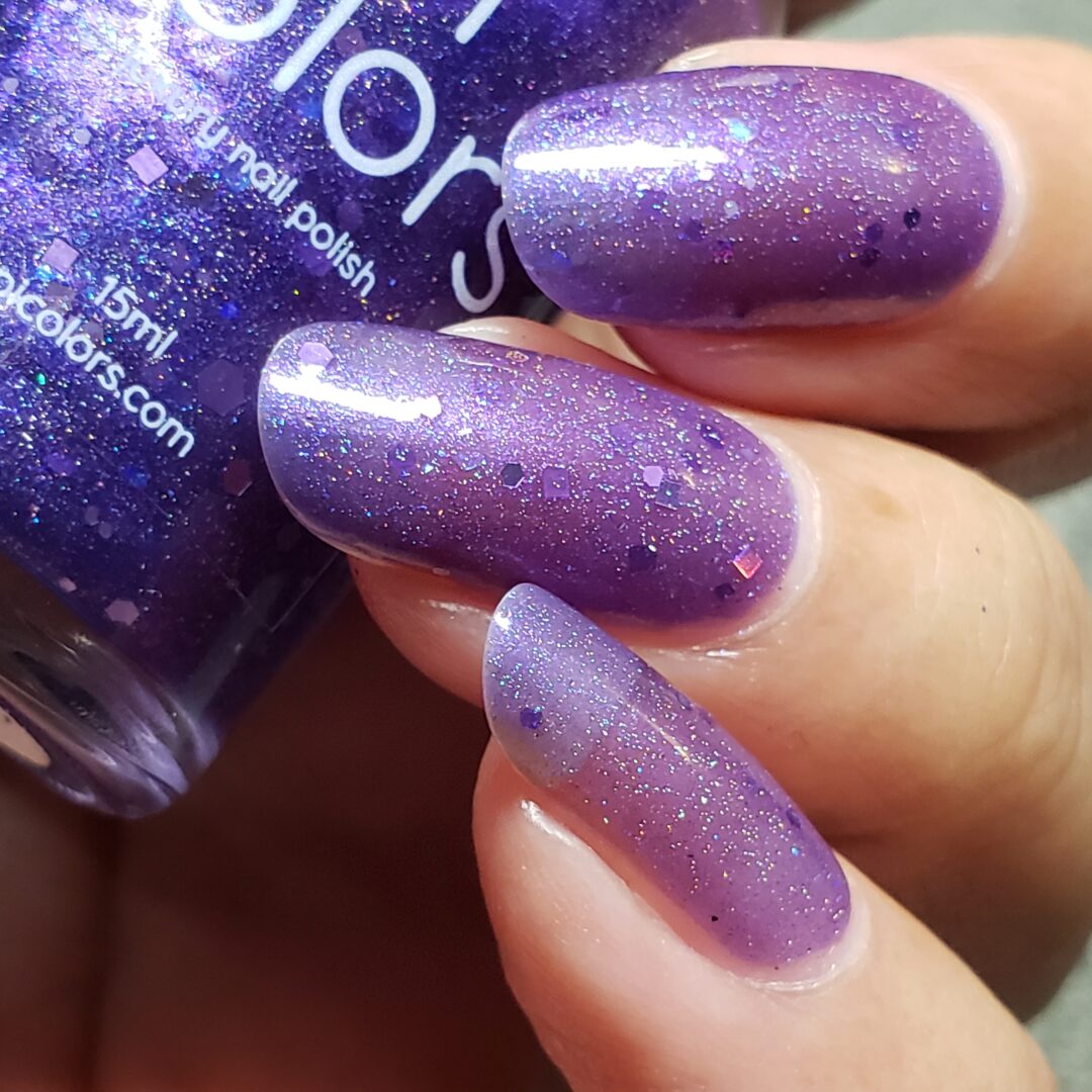 Close-up of a hand showcasing nails adorned with Purple Smoke.001, a glittery holo purple nail polish. The PI Colors Luxury Nail Lacquers polish features a slightly translucent formula with a sparkly, textured finish. A bottle of this same purple jelly polish can be seen in the background.