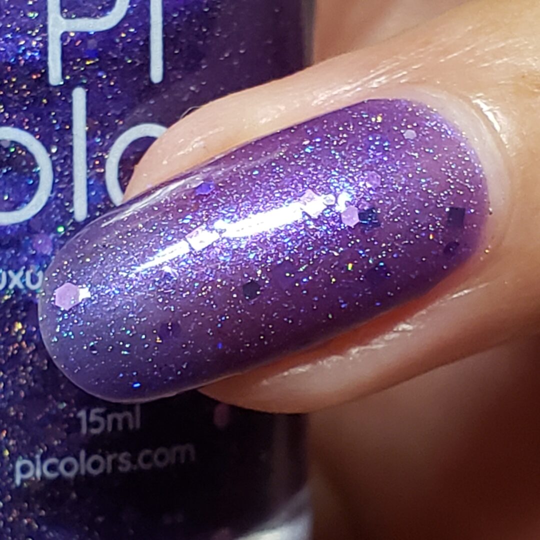 A close-up of a fingernail adorned with Purple Smoke.001, a vibrant jelly polish featuring PI Colors' signature holographic purple glitters. The dazzling effect is amplified by tiny reflective particles, set against the backdrop of a bottle of PI Colors Purple Smoke.001 Luxury Nail Lacquer in the same captivating hue.