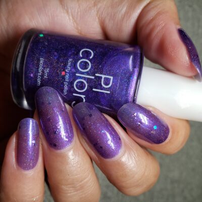 Close-up of a hand with long nails painted in PI Colors' Purple Smoke.001 nail polish, showcasing a shimmering purple finish. The hand holds a small bottle of the same color, adorned with dazzling holo purple glitters. The background is a soothing neutral tone.