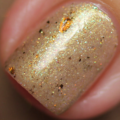 Close-up of a fingernail adorned with PI Colors' Golden King.001 Gold Nail Polish, showcasing shimmering gold and iridescent foil. The smooth surface is highlighted with specks of gold and holographic glitter, reflecting a spectrum of colors under light.