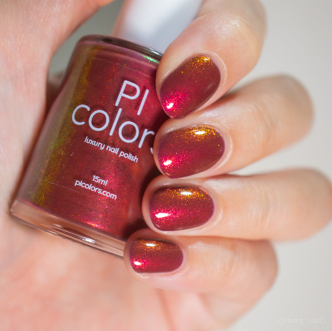 A hand holds a bottle of PI Colors Autumnal Equinox.100 luxury nail polish (15ml). The nails are painted in a warm red-brown shade with a gold-shifting shimmer.