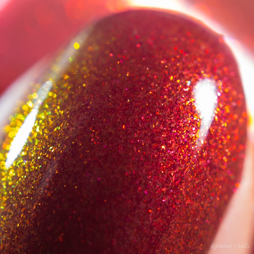 Close-up of a fingernail painted with PI Colors' Autumnal Equinox.100, a handmade color-shifting shimmer nail polish that transitions from warm red-brown to gold for a sparkling, glossy finish under bright light.