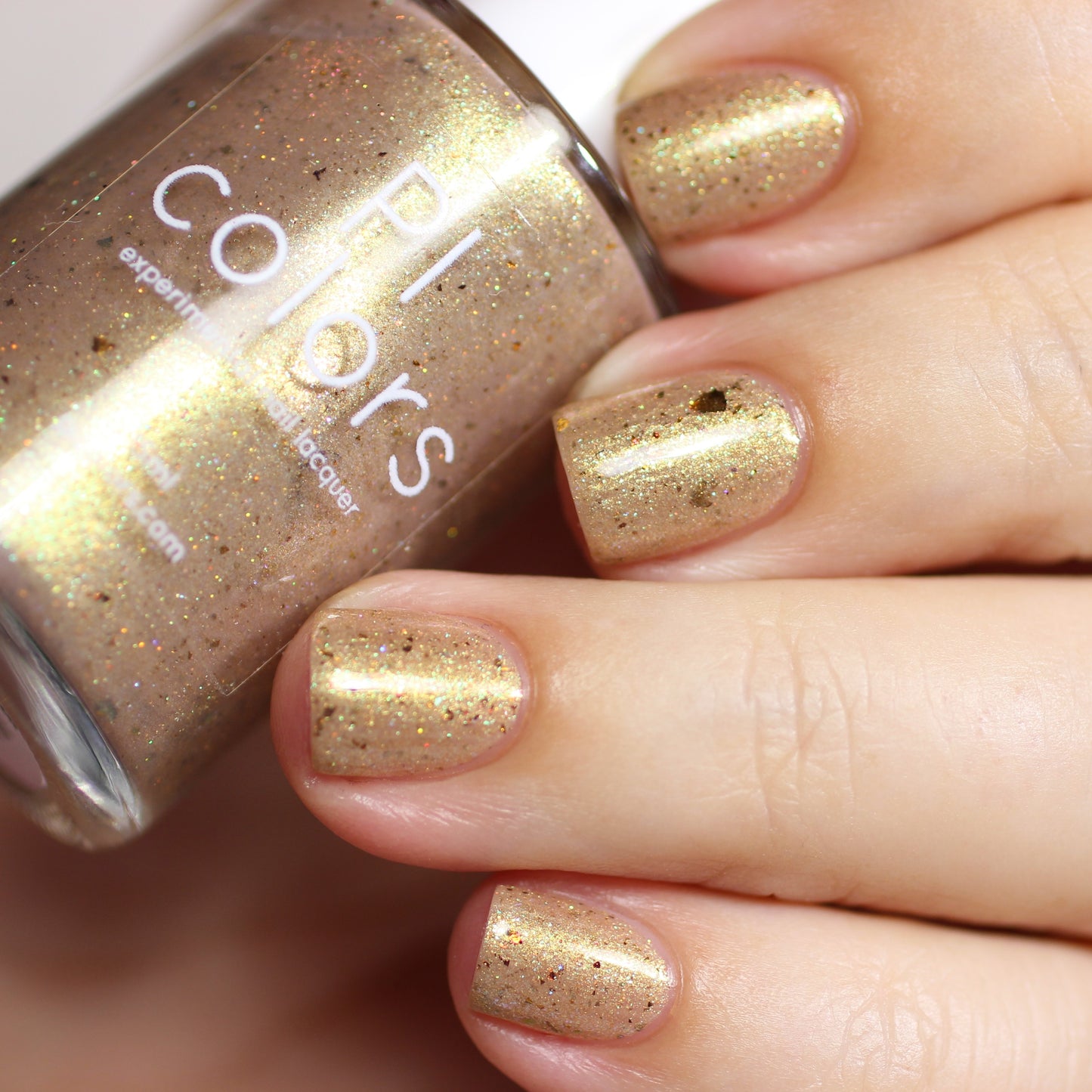 A close-up shows fingers adorned with metallic gold nail polish, accentuated by holographic glitter. The hand is holding a bottle of "Golden King.001" nail lacquer from PI Colors.