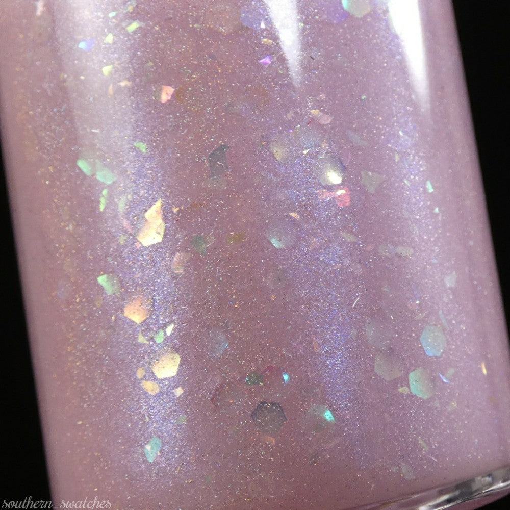 Close-up of a PI Colors "Special Week.000 Pink" nail polish bottle, showcasing a pastel lavender shade enhanced with iridescent glitters and a shimmery finish. The glitters reflect blue, pink, and gold hues, creating a sparkling effect against the smooth surface.