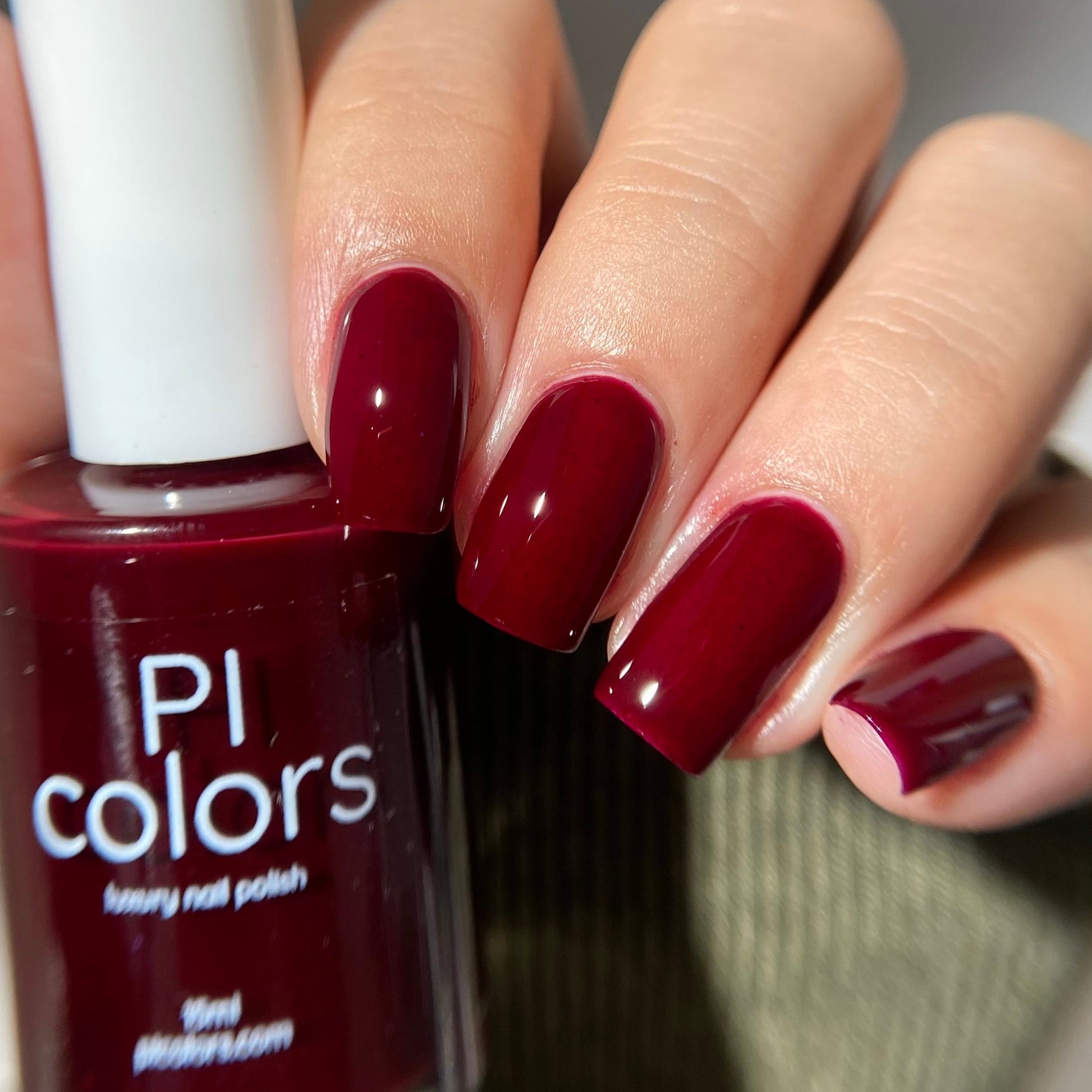 Maroon nail polish with a hand holding the bottle, showing matching nails.