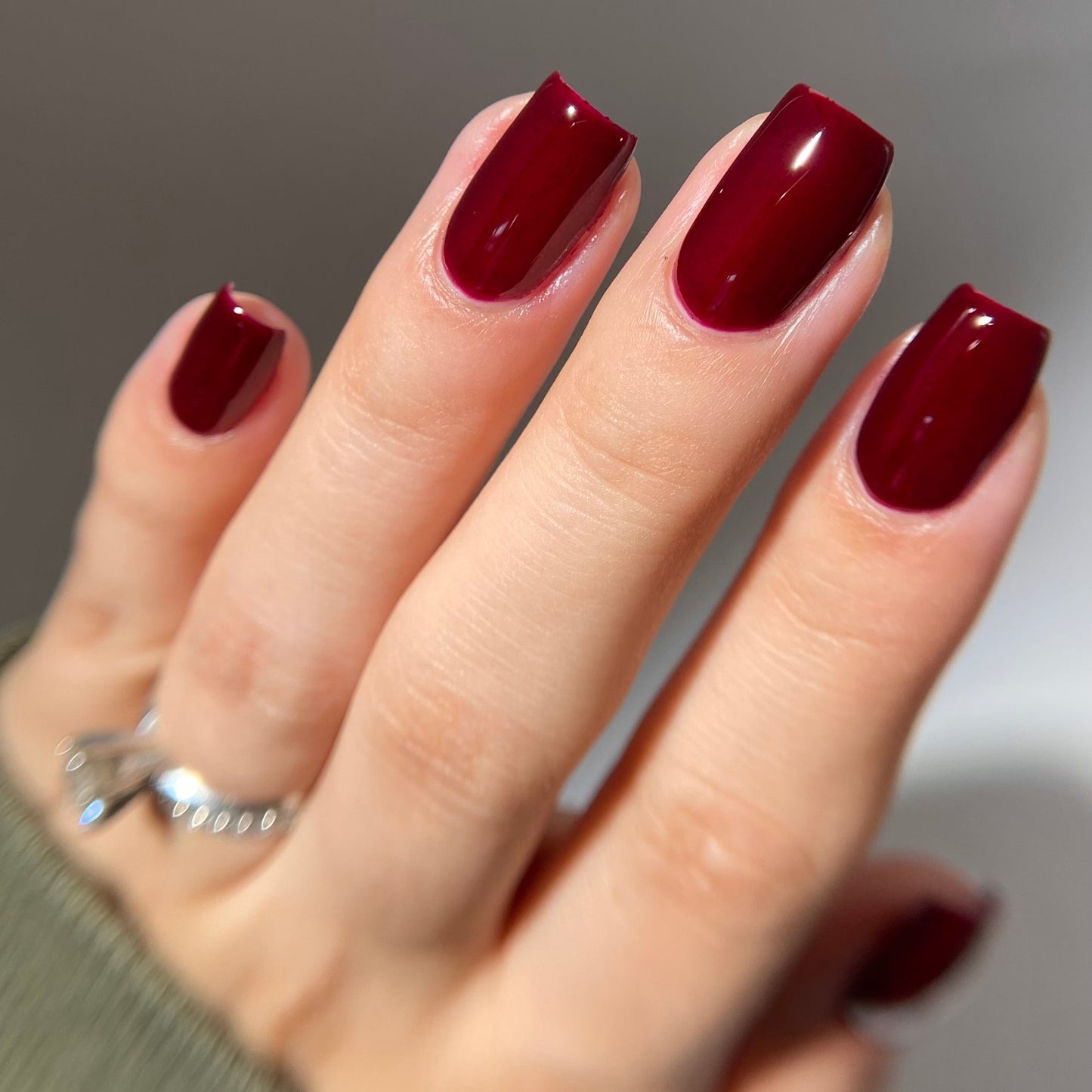 Hand with burgundy nail polish on a neutral background