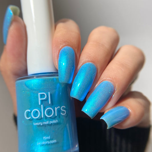 Blue nail polish bottle held by a hand with matching blue nails against a neutral background