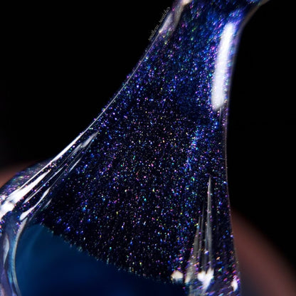 A close-up of "Judge None Choose One.000," a thick and glittery blue slime by PI Colors, being stretched evokes 90s nostalgia with its sparkling specks of purple and white reminiscent of luxurious nail lacquers. The glossy texture stands out against a dark background, amplifying the vibrant colors.