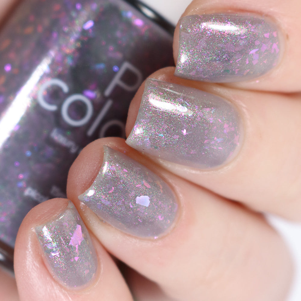 A close-up shot of a hand with short, well-manicured nails reveals the stunning "The First Rule.000 Gray Nail Polish" by PI Colors, serving as a base. The iridescent flakies create a multicolored, sparkling effect under the light for a dazzling appearance.