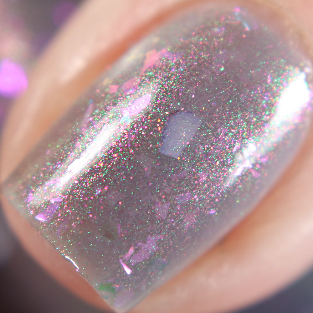 A close-up of a fingernail adorned with The First Rule.000 Gray Nail Polish by PI Colors, showcasing pink and green sparkles alongside custom batches of iridescent flakies. The glossy finish captures the light, emphasizing the multi-dimensional effect.