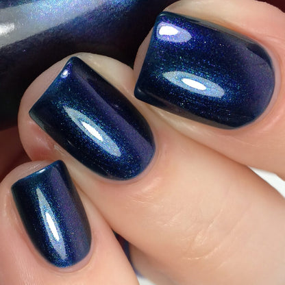 A close-up showcases polished nails with Judge None Choose One.000, a luxurious deep blue multichrome nail polish from PI Colors. The glossy finish reflects light with a shiny, smooth appearance that evokes 90s nostalgia, as it shifts between stunning shades of blue and purple under different lighting conditions.