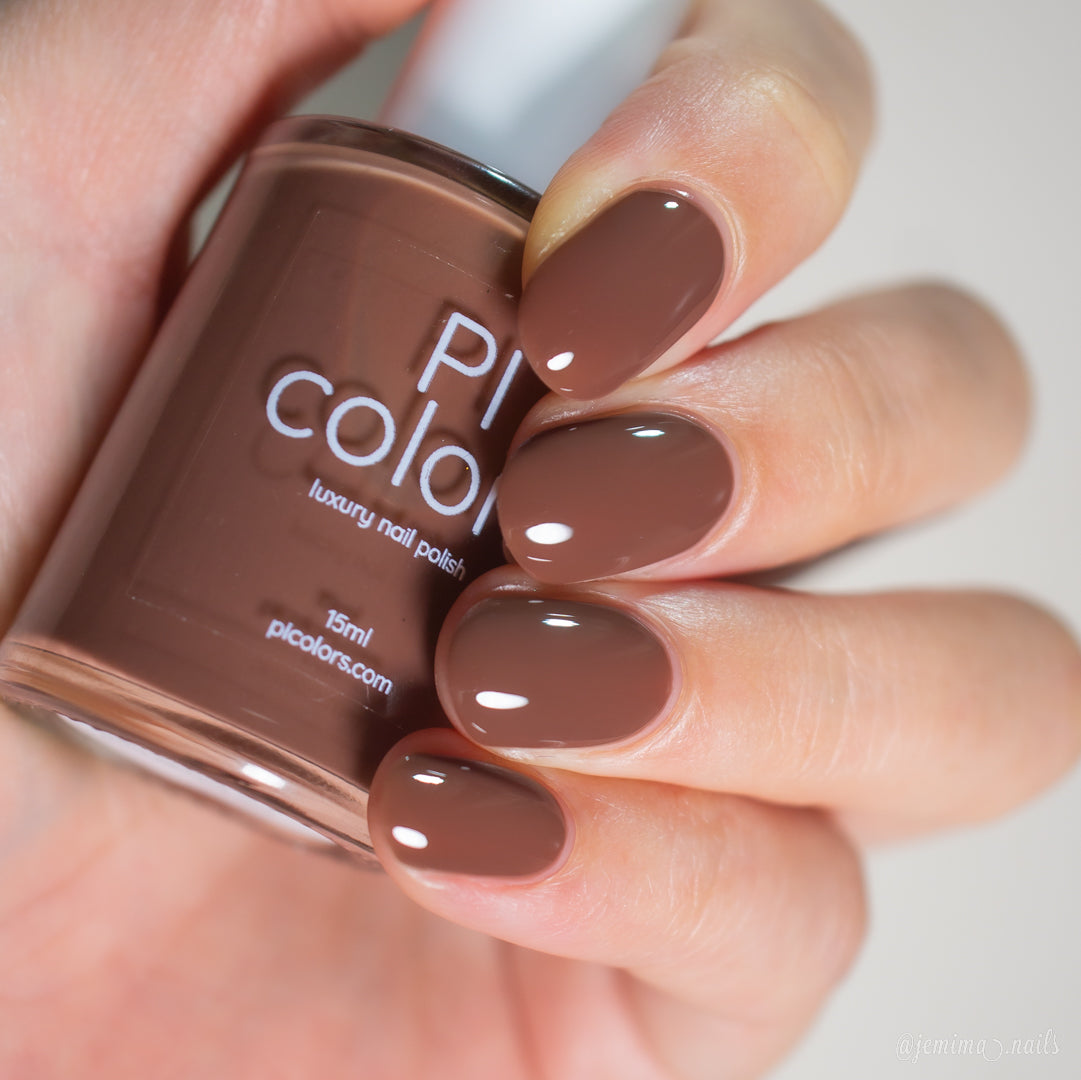 A hand with short, almond-shaped nails painted in glossy chocolate brown holds a matching "PI Colors" bottle labeled "Chocolate Turtle.411," showcasing its rich creme finish.