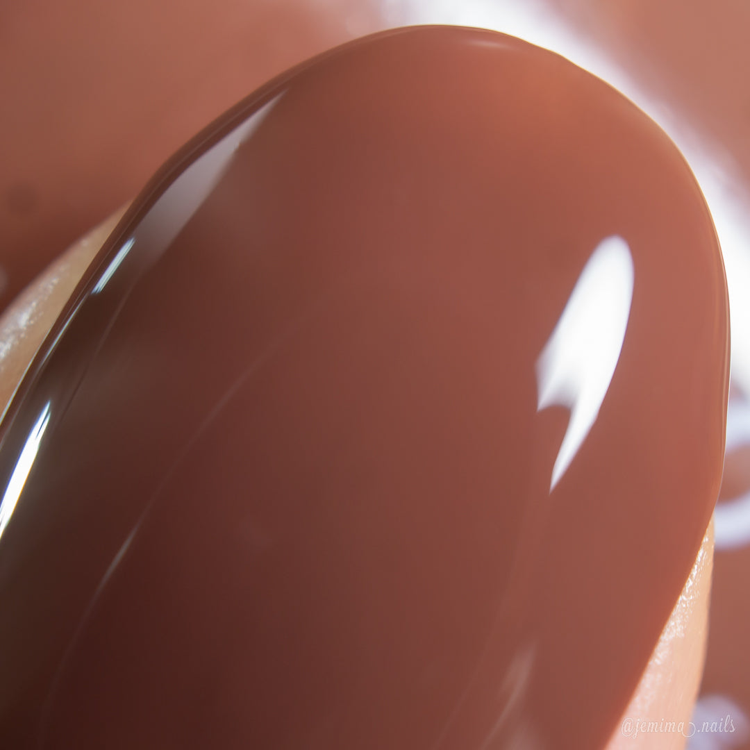 A close-up of a fingernail painted with PI Colors Chocolate Turtle.411, a chocolate brown nail polish with a shiny, smooth creme finish that reflects light.