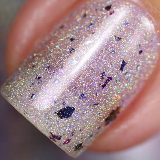 Close-up of a fingernail with PI Colors Crescent in Ice.018 Silver Nail Polish. The polish, in a silvery lilac hue, is adorned with iridescent sparkles and multichrome flakies, producing a shimmering, holographic effect on the nail.