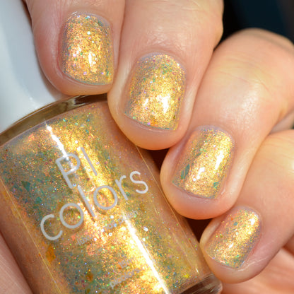 Close-up of a hand with glittery gold nail polish holding a bottle of 'PI colors' nail polish.
