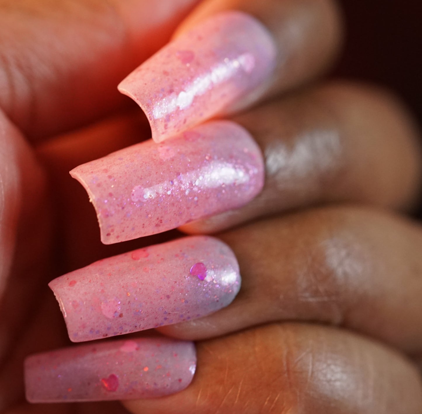 Close-up of a hand with long nails featuring Pink Berry Heart.200 by PI Colors, showcasing a gradient effect with pink glitter, holographic heart-shaped details, and a glossy 10-free finish against a blurred background.