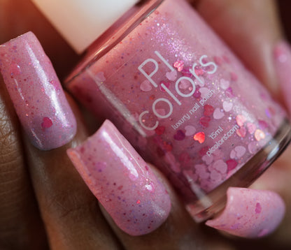 A close-up features a hand holding a bottle of PI Colors "Pink Berry Heart.200" nail polish. The nails shine with the same 10-free pale pink polish, showcasing a mix of small and large glitter pieces.