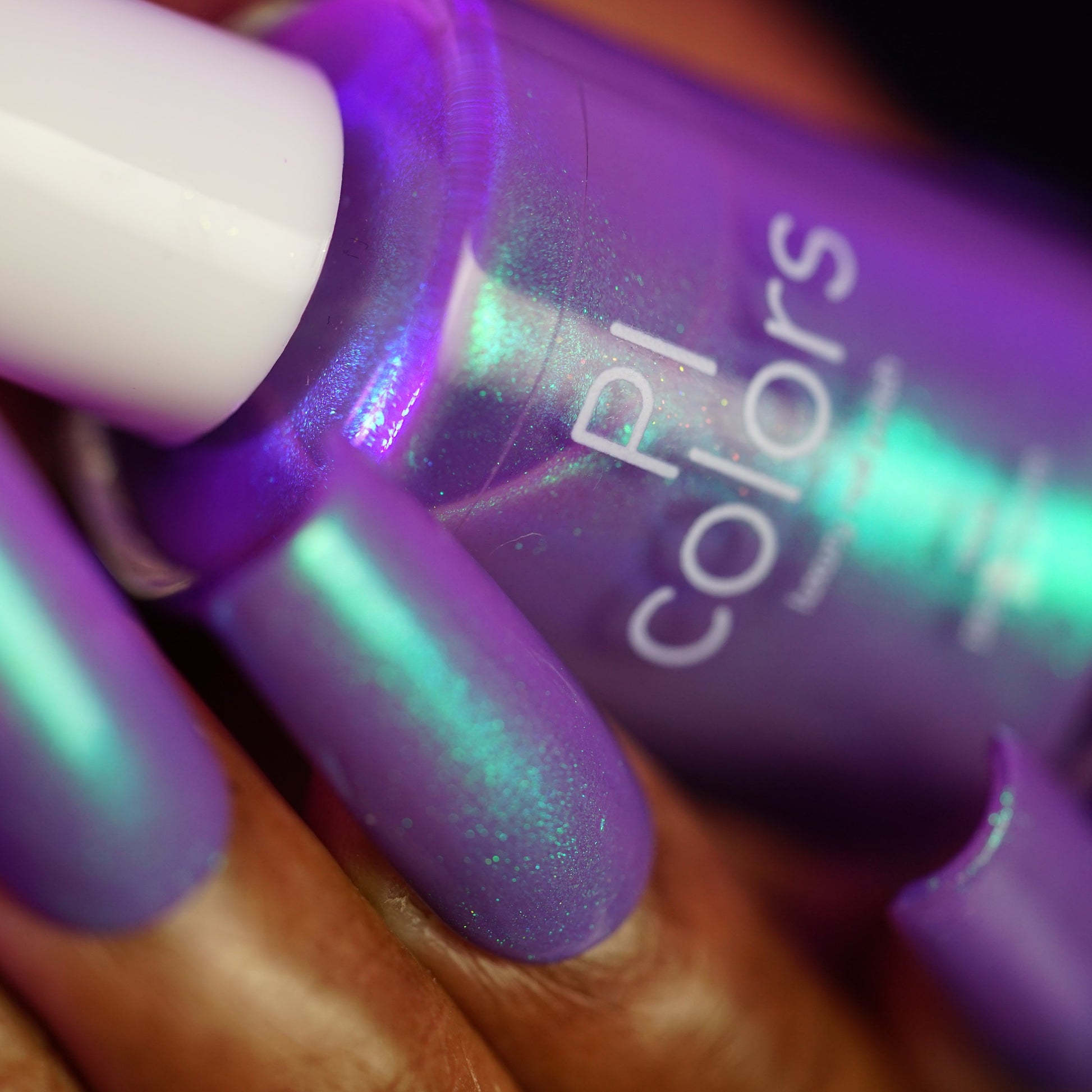 Close-up of a hand with purple nail polish holding a purple nail polish bottle.