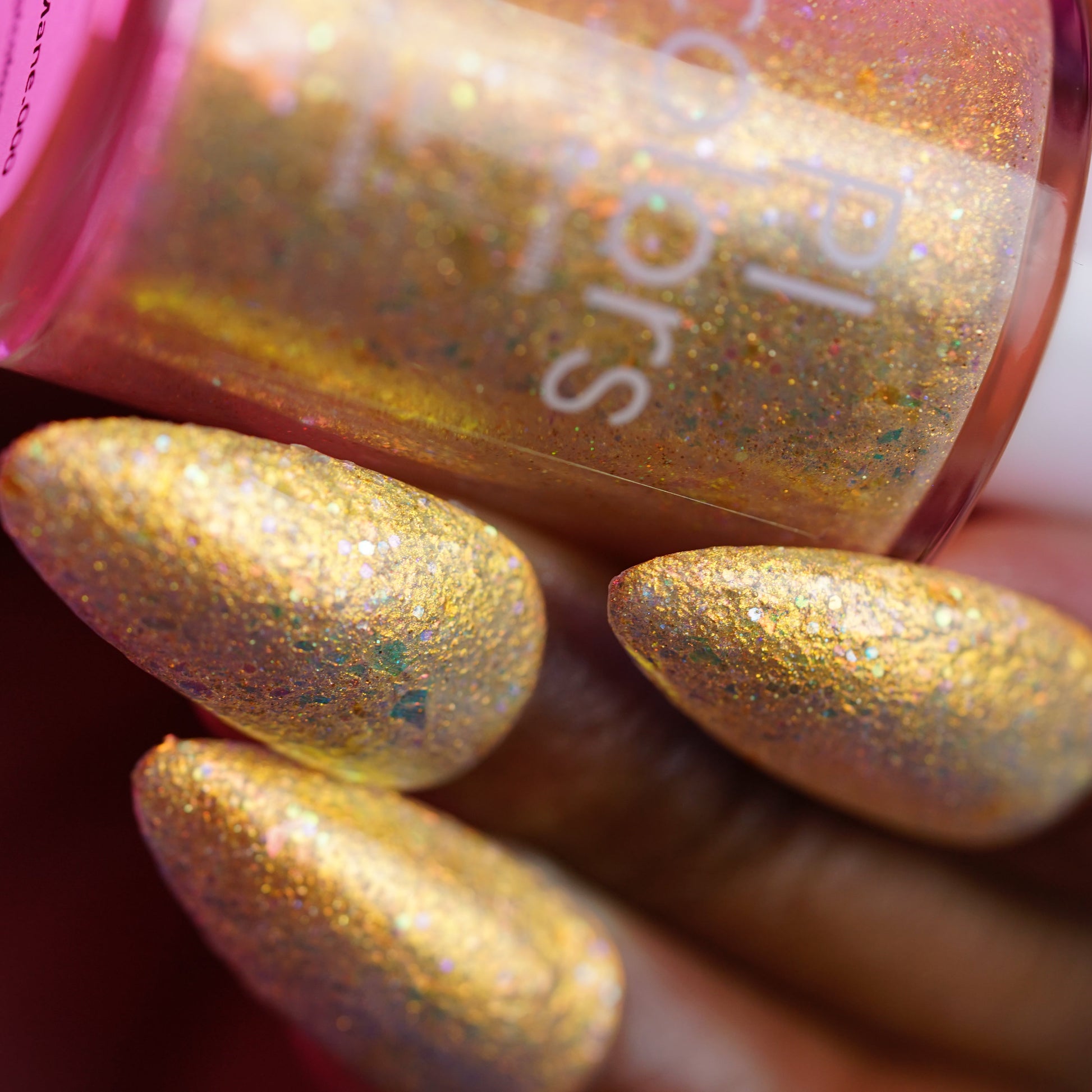 Close-up of a hand with gold glittery nail polish holding a bottle of Sally Hansen nail polish.