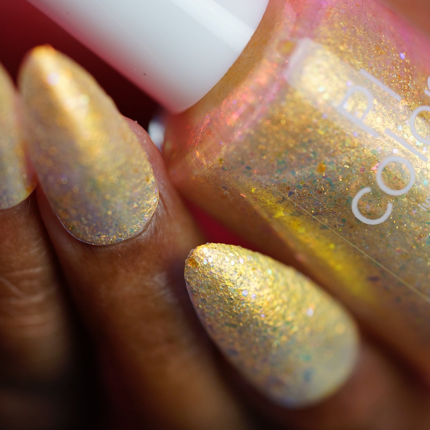 Gold glitter nail polish with a hand holding the bottle, blurred background