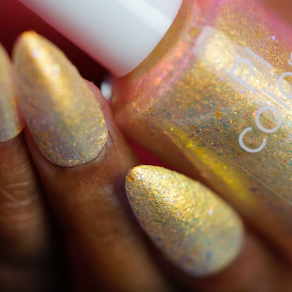 Gold glitter nail polish with a hand holding the bottle, blurred background