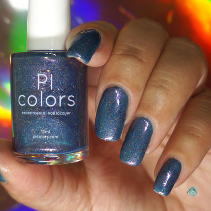 A hand showcases nails painted in "East of the Storm.029 Blue Nail Polish" by PI Colors, with a subtle glitter finish. The bottle is elegantly held between the fingers, highlighting its color-shifting iridescent flakies. A vibrant, blurred background enhances the colorful scene.